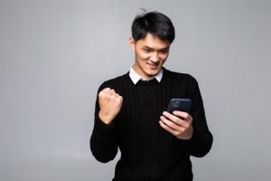 retrato-joven-asiatico-ve-feliz-mientras-lee-buena-noticia-telefono-inteligente-pared-blanca_231208-1574-300x200